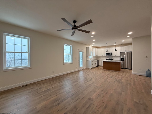 kitchen featuring a center island, decorative light fixtures, a healthy amount of sunlight, white cabinetry, and stainless steel appliances