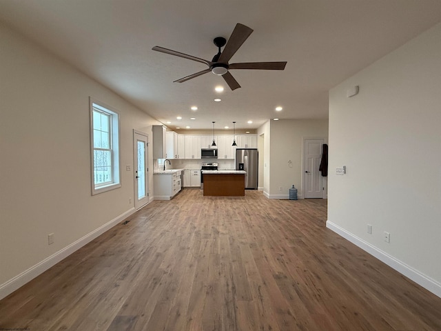 unfurnished living room featuring wood-type flooring, ceiling fan, and sink