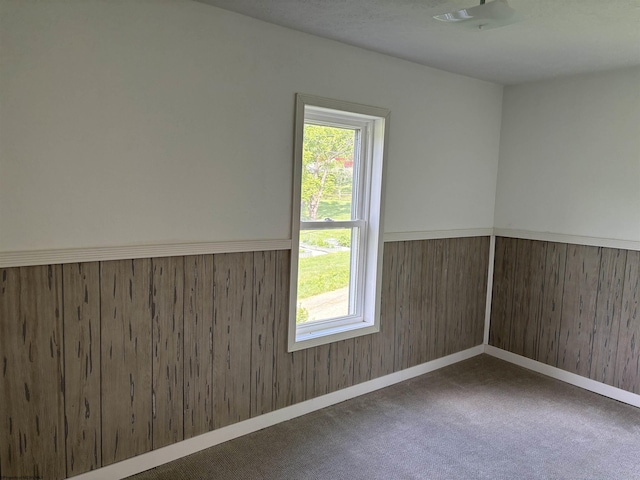 unfurnished room featuring dark carpet, a textured ceiling, and wooden walls