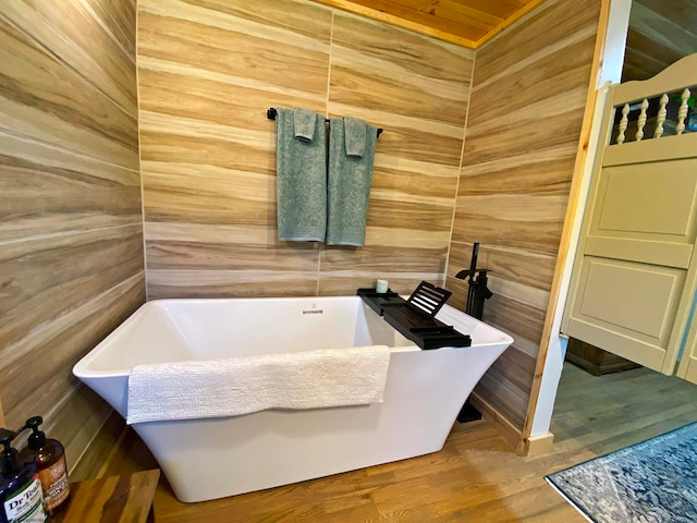 bathroom with a bath, wood-type flooring, and wooden walls