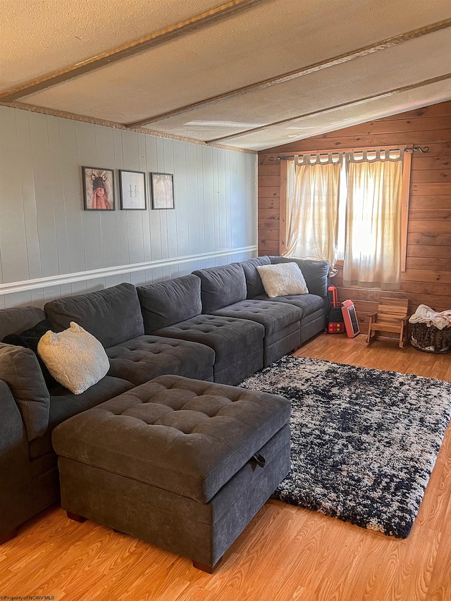 living room with light hardwood / wood-style floors, a textured ceiling, wood walls, and vaulted ceiling