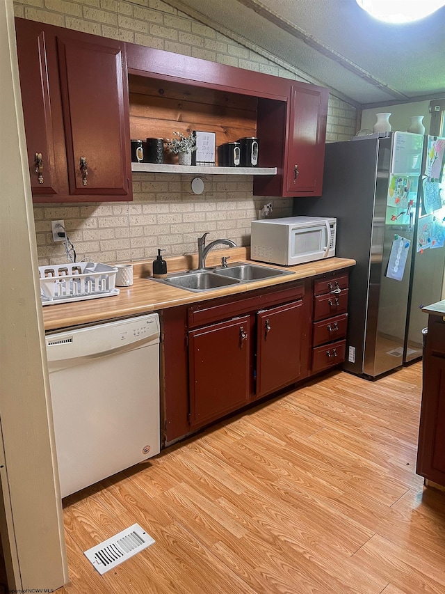 kitchen with brick wall, vaulted ceiling, light hardwood / wood-style floors, sink, and white appliances