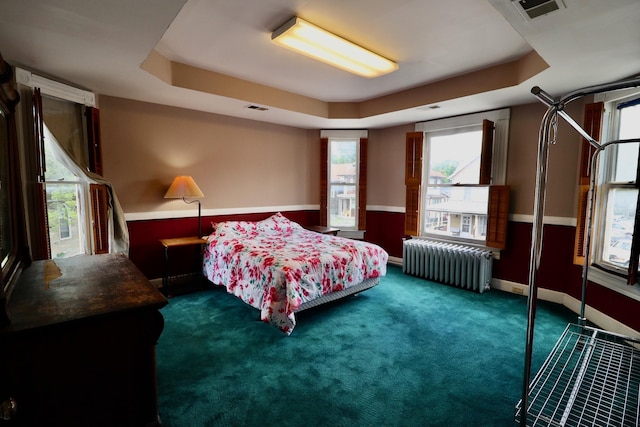 carpeted bedroom featuring a raised ceiling and radiator