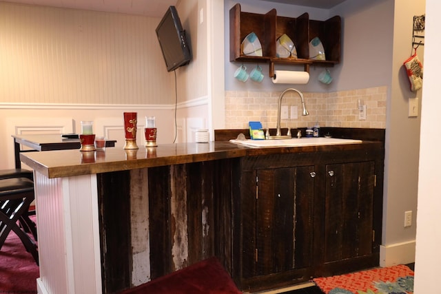 bar with backsplash, dark brown cabinetry, and sink