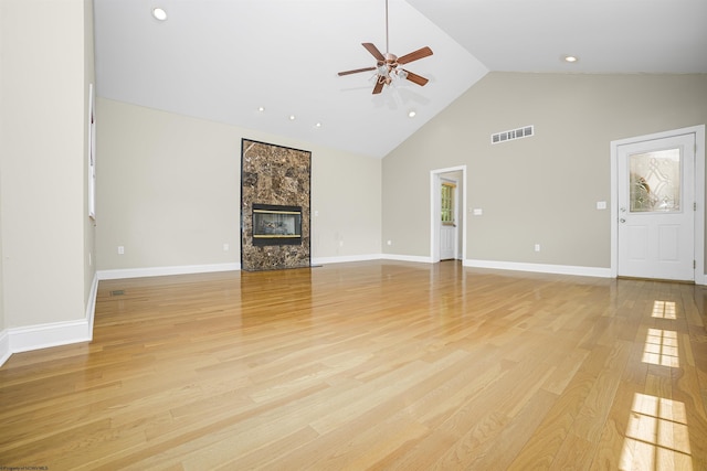 unfurnished living room with a premium fireplace, light hardwood / wood-style flooring, high vaulted ceiling, and ceiling fan