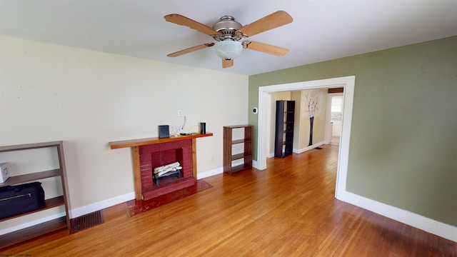 living room featuring hardwood / wood-style floors, ceiling fan, and a brick fireplace