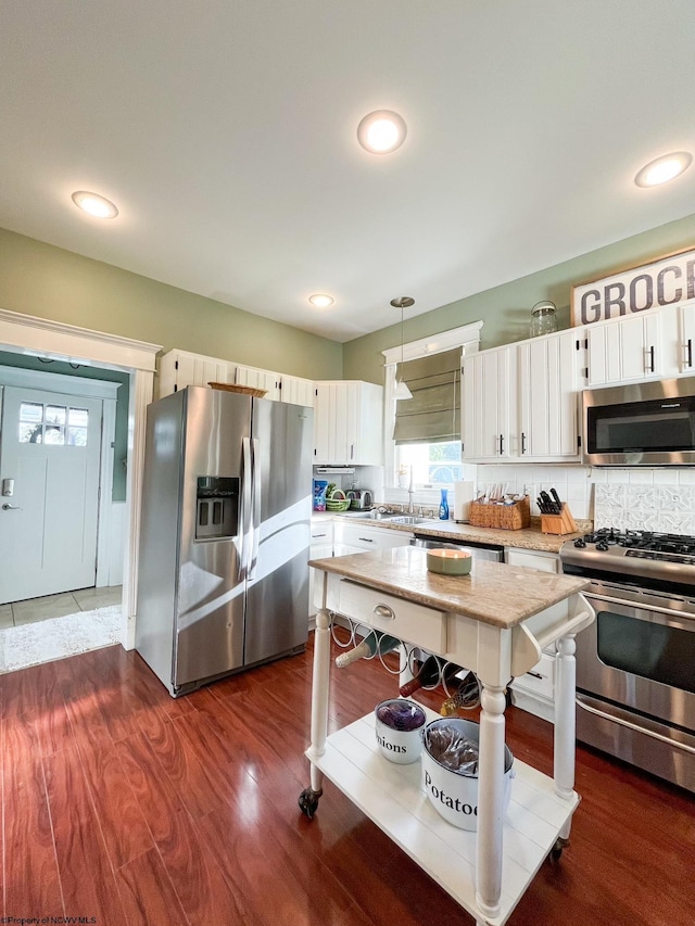 kitchen with dark hardwood / wood-style flooring, backsplash, stainless steel appliances, white cabinets, and hanging light fixtures