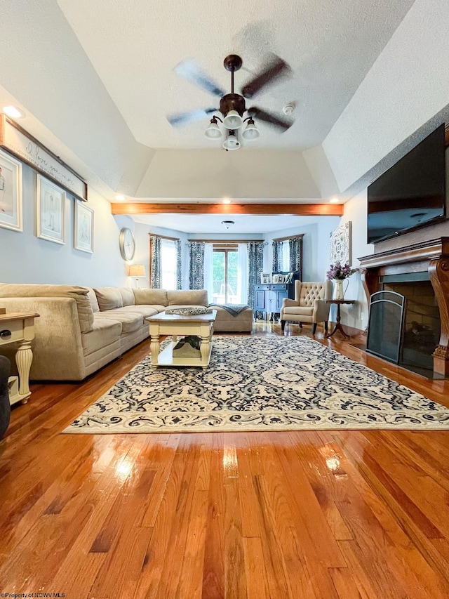 living room with hardwood / wood-style floors, lofted ceiling, ceiling fan, a textured ceiling, and a tray ceiling