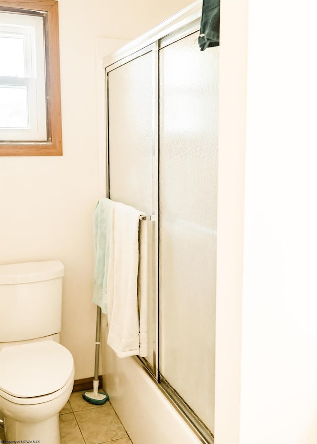 bathroom with tile patterned flooring, toilet, and combined bath / shower with glass door