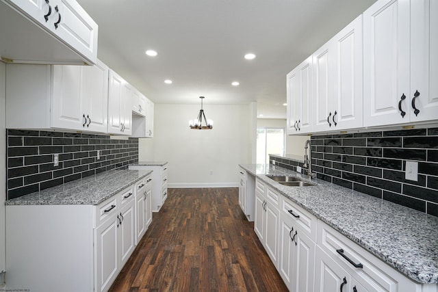 kitchen featuring sink, light stone countertops, decorative light fixtures, dark hardwood / wood-style flooring, and white cabinetry