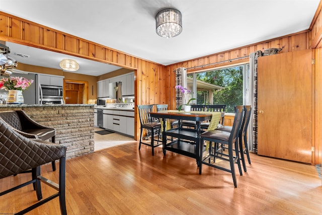 dining area with wood walls, a notable chandelier, and light hardwood / wood-style floors