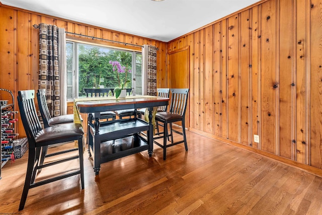 dining space with hardwood / wood-style flooring, crown molding, and wood walls