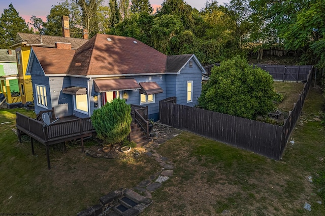 back house at dusk with a deck and a lawn