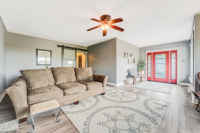 living room featuring crown molding, ceiling fan, a barn door, and light hardwood / wood-style flooring