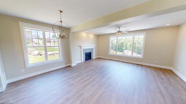 unfurnished living room featuring plenty of natural light, light hardwood / wood-style floors, a fireplace, and ceiling fan with notable chandelier