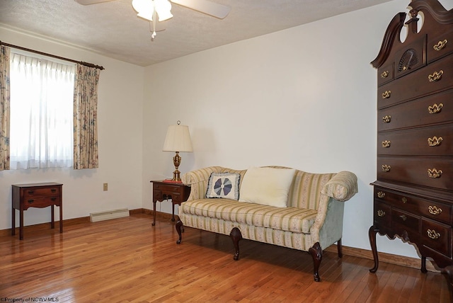 living area with ceiling fan, a textured ceiling, hardwood / wood-style flooring, and baseboard heating