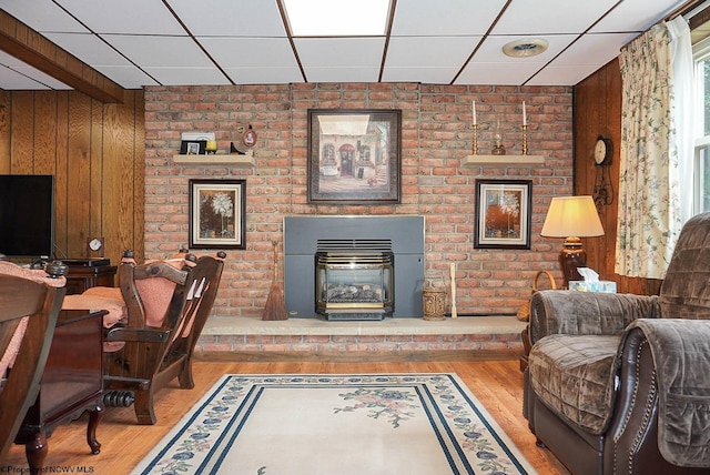 living room with brick wall, a fireplace, wood walls, a drop ceiling, and hardwood / wood-style floors