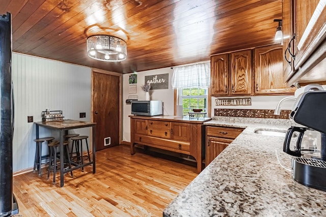 kitchen featuring sink, fridge, light hardwood / wood-style floors, light stone counters, and wood ceiling