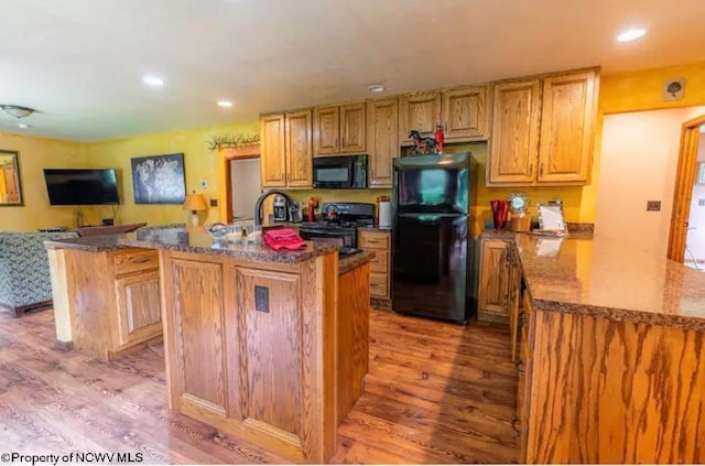 kitchen featuring dark stone countertops, a kitchen island with sink, black appliances, and light hardwood / wood-style floors