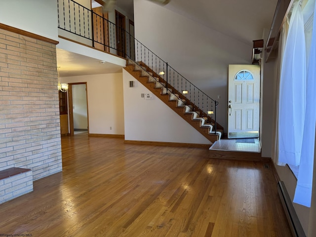 entrance foyer with hardwood / wood-style floors, a baseboard radiator, a high ceiling, and a notable chandelier