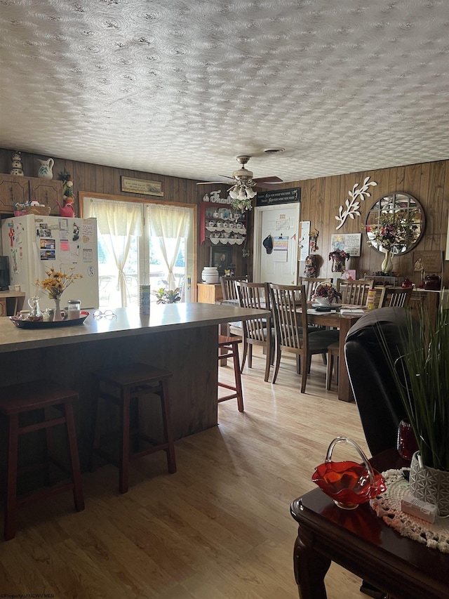 dining area featuring wood walls, ceiling fan, light hardwood / wood-style floors, and a textured ceiling