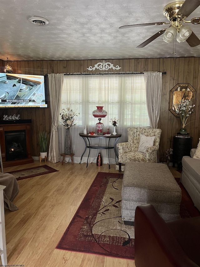 living area featuring wood walls, ceiling fan, wood-type flooring, and a textured ceiling