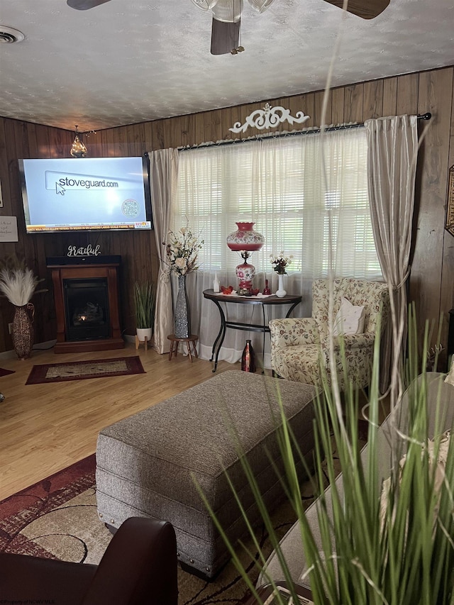 living room featuring ceiling fan, wooden walls, wood-type flooring, and a textured ceiling