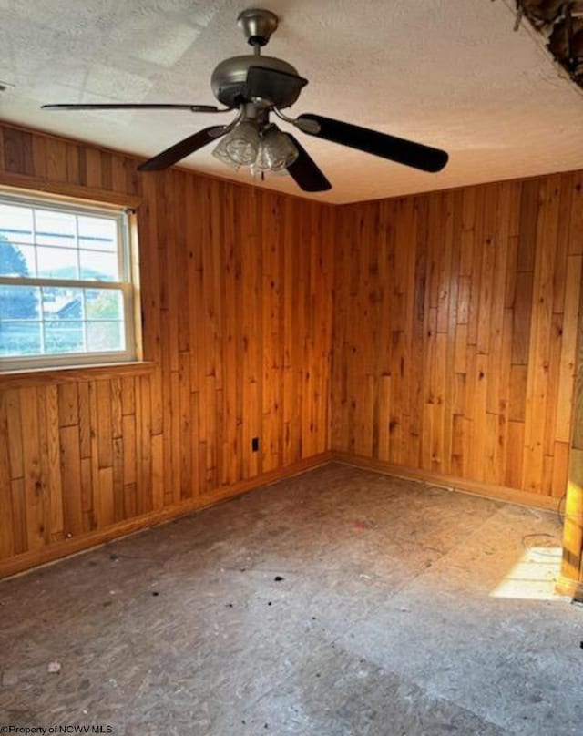 empty room with wooden walls, a textured ceiling, and ceiling fan