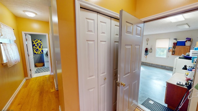 corridor with light hardwood / wood-style floors, a textured ceiling, and washer / dryer