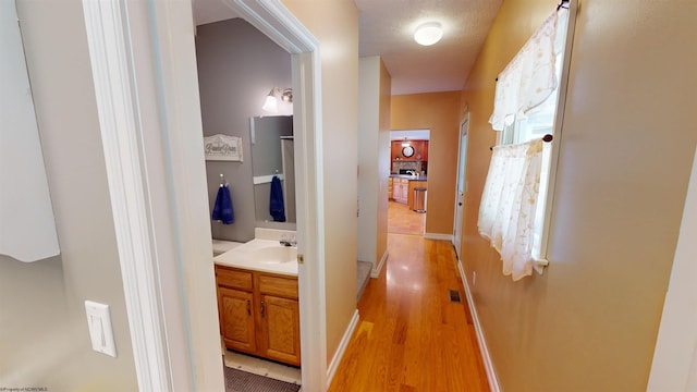 hall featuring a textured ceiling, light wood-type flooring, and sink