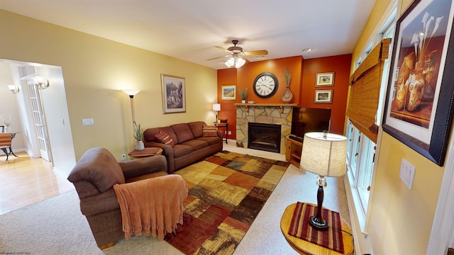 living room featuring carpet, ceiling fan, and a stone fireplace