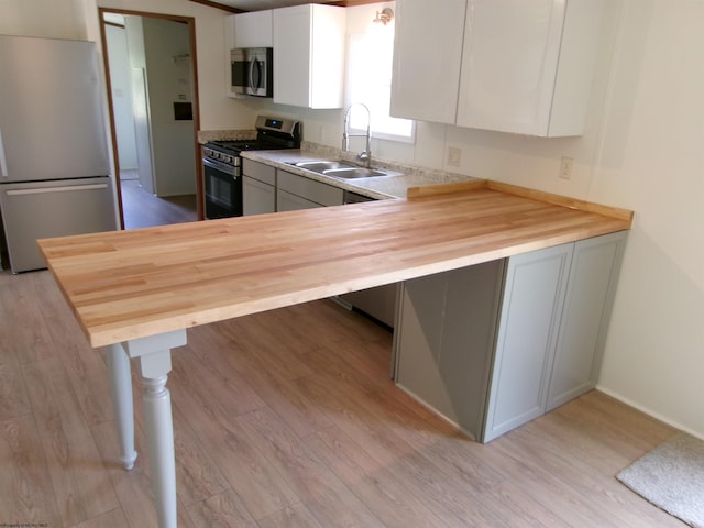 kitchen featuring butcher block counters, light wood-type flooring, appliances with stainless steel finishes, white cabinets, and a sink