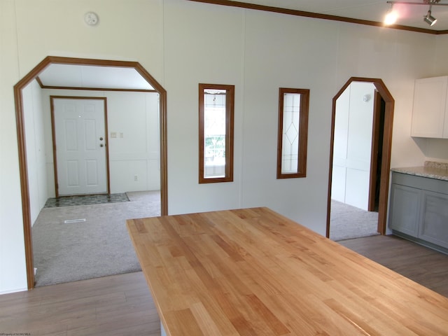 foyer featuring arched walkways, ornamental molding, light wood-style floors, a towering ceiling, and light colored carpet