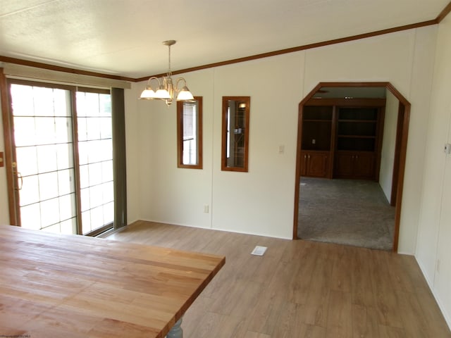 unfurnished dining area with an inviting chandelier, crown molding, wood finished floors, and arched walkways