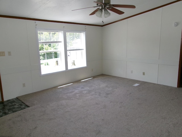 carpeted empty room with ornamental molding, a ceiling fan, and a decorative wall