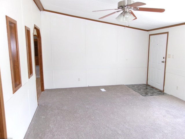 empty room with a decorative wall, ceiling fan, crown molding, and carpet