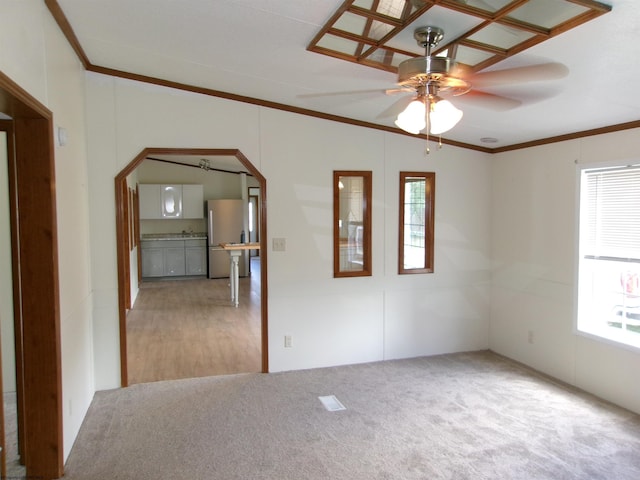 carpeted empty room with a ceiling fan, a healthy amount of sunlight, arched walkways, and ornamental molding