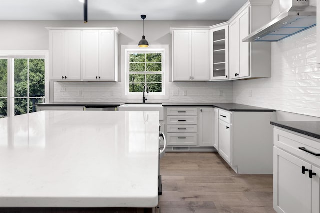 kitchen featuring wall chimney exhaust hood, sink, decorative light fixtures, light hardwood / wood-style flooring, and white cabinets