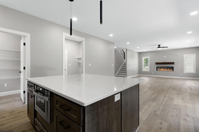 kitchen with dark brown cabinetry, ceiling fan, light hardwood / wood-style flooring, a kitchen island, and hanging light fixtures