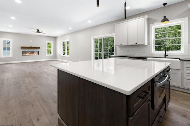 kitchen featuring light wood-type flooring, tasteful backsplash, sink, decorative light fixtures, and white cabinetry