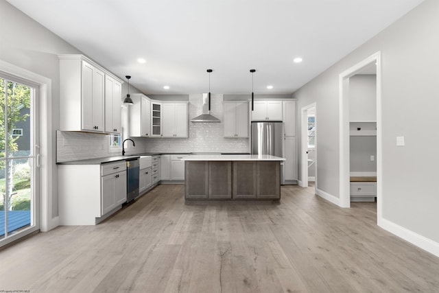 kitchen featuring stainless steel appliances, wall chimney range hood, pendant lighting, white cabinetry, and a kitchen island