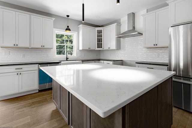 kitchen featuring stainless steel appliances, sink, wall chimney range hood, a kitchen island, and hanging light fixtures