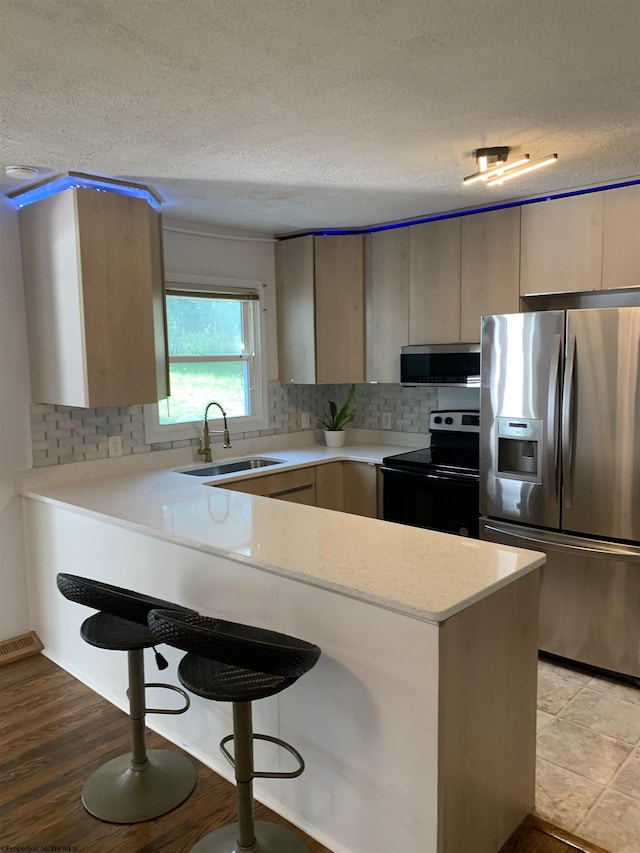 kitchen with a textured ceiling, appliances with stainless steel finishes, a kitchen bar, sink, and kitchen peninsula