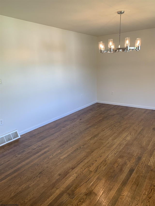 spare room with an inviting chandelier and dark hardwood / wood-style floors