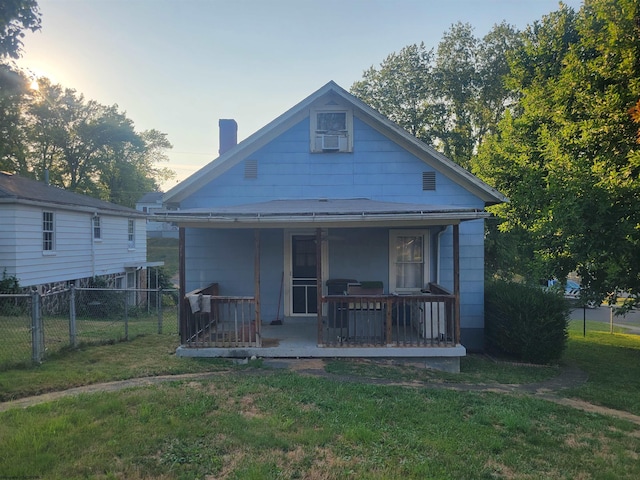 back house at dusk featuring a yard and covered porch