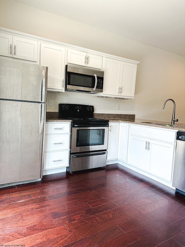 kitchen featuring dark wood-type flooring, white cabinetry, stainless steel appliances, dark stone counters, and sink