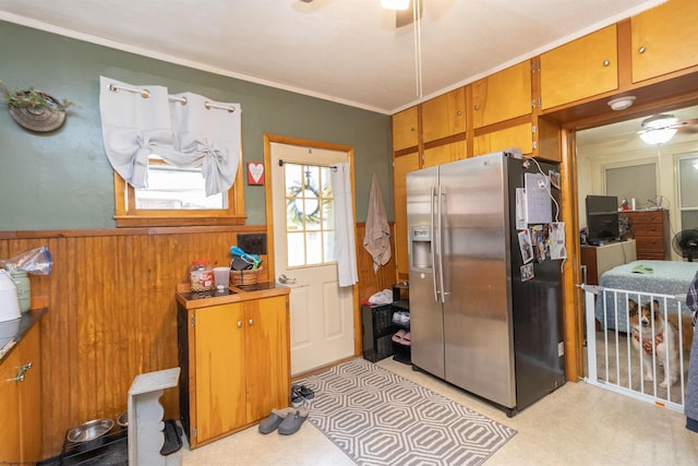 kitchen featuring stainless steel refrigerator with ice dispenser, crown molding, ceiling fan, and wooden walls