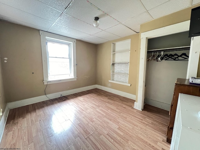 unfurnished bedroom with light wood-type flooring, a closet, and a drop ceiling