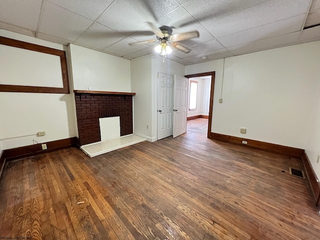 unfurnished living room with hardwood / wood-style floors, a brick fireplace, ceiling fan, and a paneled ceiling