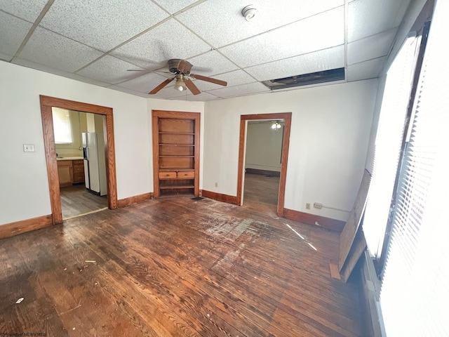 unfurnished bedroom with a drop ceiling, white fridge, wood-type flooring, ceiling fan, and ensuite bathroom